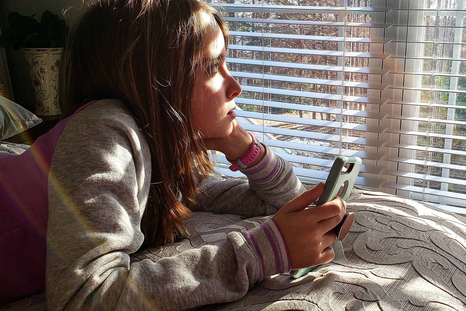 A young girl stares out the window whilst holder her phone A young girl stares out the window whilst holder her phone
